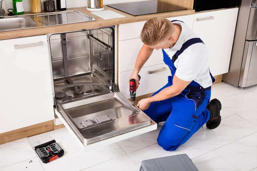 Technician in overalls repairing an open dishwasher with a screwdriver