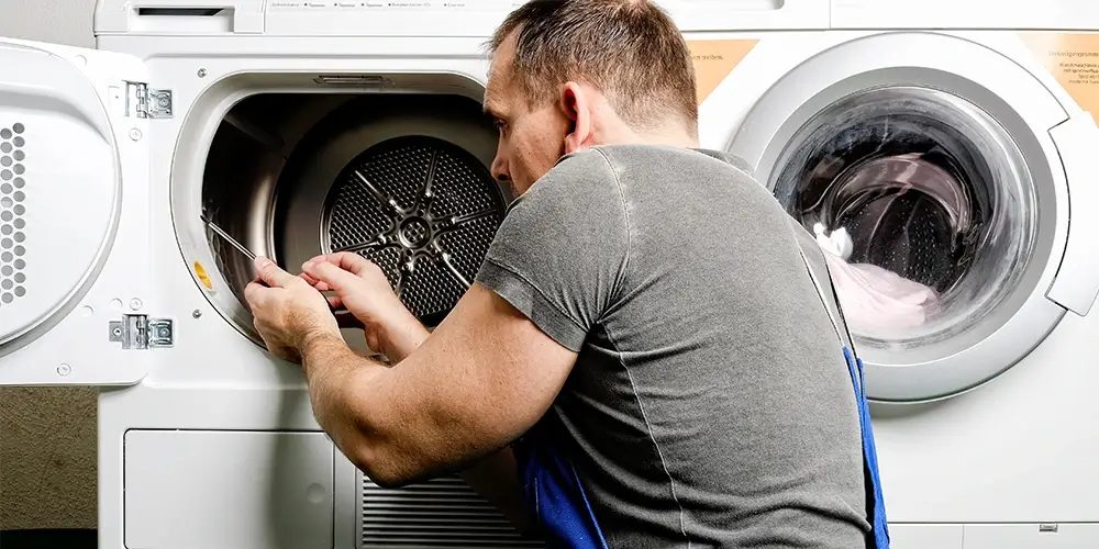 Technician reaching into an open dryer drum in a laundry room
