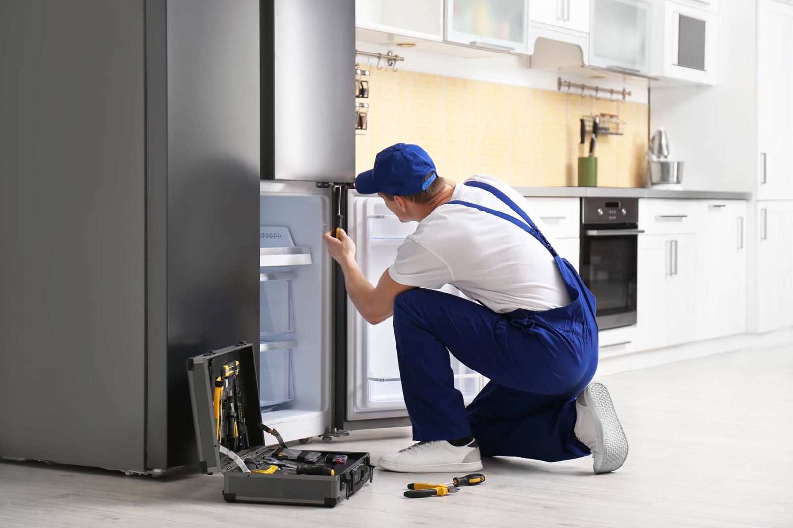 Technician kneeling at an open refrigerator with a tool case beside him