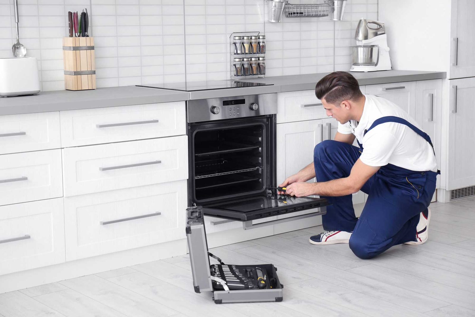 Technician working on an open wall oven in a white kitchen